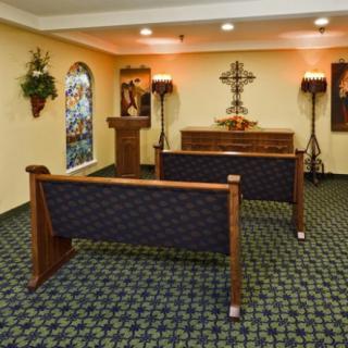 A small chapel with wooden pews facing an altar, adorned with a cross and flanked by floral arrangements.