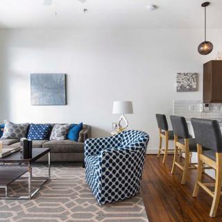 A modern living room featuring a stylish sofa, a patterned armchair, and bar stools at the kitchen counter.
