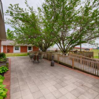 A spacious backyard with a paved patio area featuring outdoor seating and a large tree, surrounded by a fence.