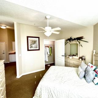 A cozy bedroom featuring a neatly made bed, ceiling fan, dresser with a mirror, and wall decorations.