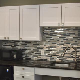 A modern kitchen setup featuring white cabinets, a tile backsplash, and a sleek countertop with a sink and faucet.