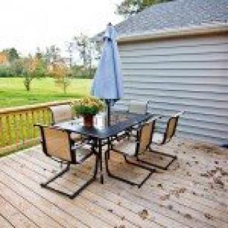 An outdoor wooden patio with a table, four chairs, and an umbrella, set in a backyard.