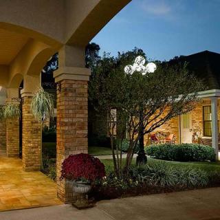 A warmly lit patio with brick columns and a well-manicured garden in the evening.