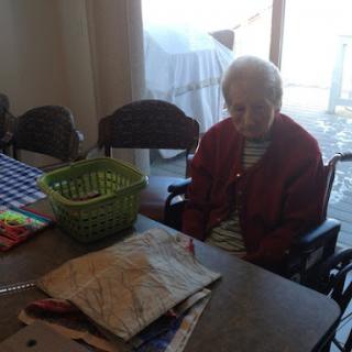 An elderly person sitting at a table with a basket in a cozy indoor setting.