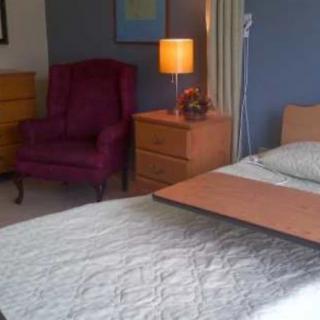 A cozy bedroom with a bed, nightstand, lamp, and an upholstered chair.