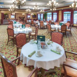 An elegant dining room with neatly arranged tables and chairs, featuring decorative lighting and a carpeted floor.