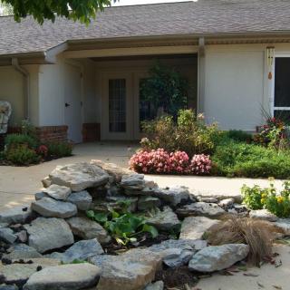 A single-story house with a landscaped front yard featuring a rock garden and surrounding greenery.