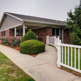 A brick residential house with neatly trimmed bushes and a white fence lining the sidewalk.