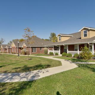 A row of suburban houses with a well-maintained lawn and winding pathway under a clear blue sky.