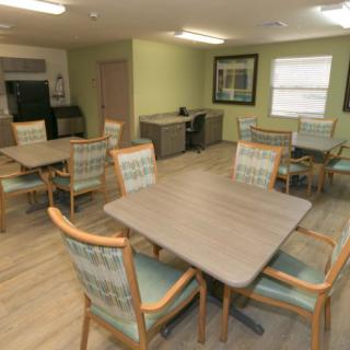 A modern dining area with multiple tables and chairs, featuring a kitchenette in the background.
