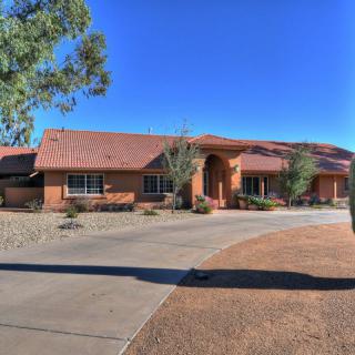 A single-story house with a wide driveway in a desert setting under a clear blue sky.