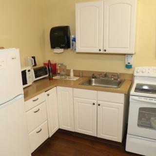 A compact kitchen with white cabinets, a stove, refrigerator, and small appliances on the countertop.