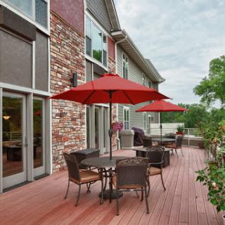 A cozy outdoor patio area featuring tables under red umbrellas, surrounded by a modern building and lush greenery.