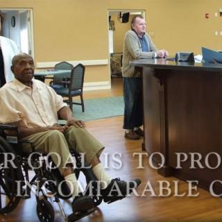 A person in a wheelchair sits near a reception desk in a nursing home.