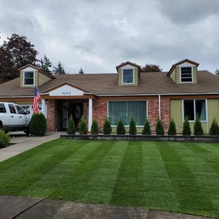 A suburban house with a well-maintained lawn and an American flag displayed, under a cloudy sky.