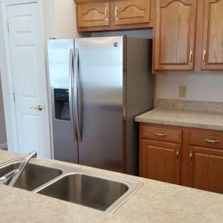 A modern kitchen with a stainless steel refrigerator, dual sink, and wooden cabinets.