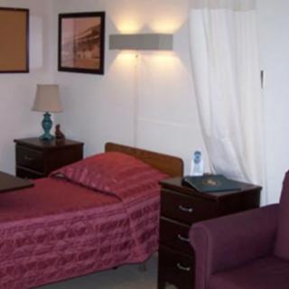 A small room with a single bed, bedside table, and lamp, suggesting a cozy or clinical setting.