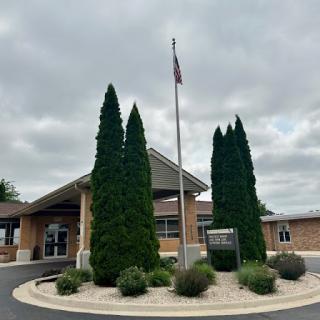 A welcoming entrance with manicured trees and an American flag under a cloudy sky.