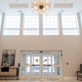 A modern lobby with large windows, a striking chandelier, and elegant decor.