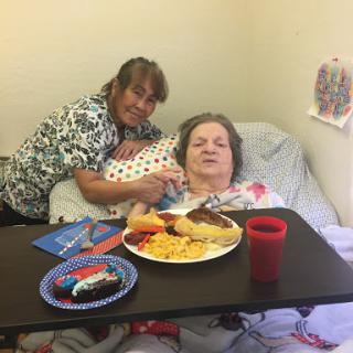 A caregiver provides companionship and a meal to an elderly person in a hospital setting.