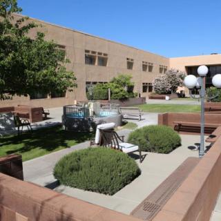 A peaceful courtyard featuring benches, greenery, and lamp posts surrounded by a building.