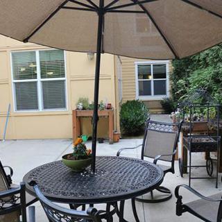 A cozy patio with a table and chairs under an umbrella, surrounded by plants.