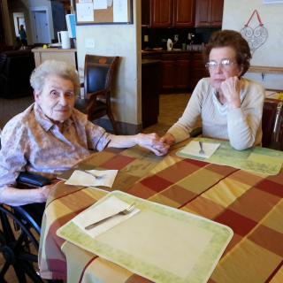 Two elderly women sit at a table, holding hands and enjoying each other's company.