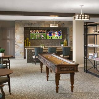 A modern game room featuring a shuffleboard table, television displaying sports, and comfortable seating areas.