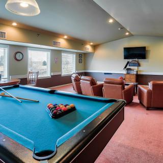 A cozy recreation room featuring a pool table and seating area with a TV.