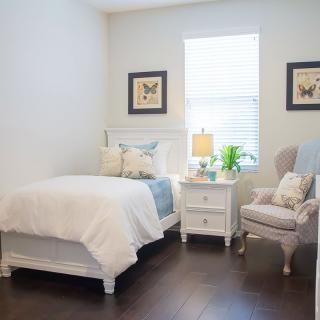 A cozy and minimalist bedroom featuring a bed, nightstand, and chair with simple decor.