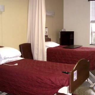 A hospital room with two beds featuring maroon covers, separated by a privacy curtain.
