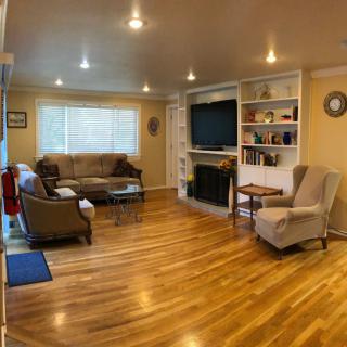A cozy living room with wood flooring, featuring a sofa, armchair, television, and a fireplace surrounded by shelves.