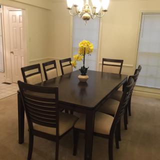 A dining room featuring a dark wooden table surrounded by eight chairs, with a decorative vase of yellow flowers under a chandelier.