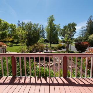 A scenic view of a lush garden from a wooden deck on a sunny day.