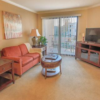 A cozy living room with a sofa, coffee table, and television, featuring a sliding glass door leading to a balcony.
