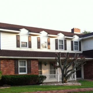 A two-story suburban house with a brick facade and white siding, featuring dormer windows and a chimney.