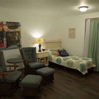 A cozy bedroom with a neatly made bed, comfortable chairs, and warm lighting.
