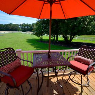 A sunny deck with patio furniture including an umbrella, chairs, and a table overlooking a green lawn.