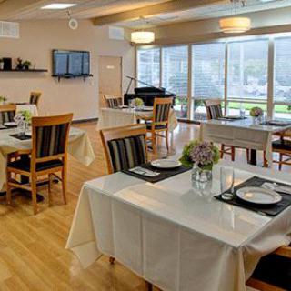 A modern and well-lit restaurant dining area with neatly arranged tables and chairs, featuring large windows and a piano.