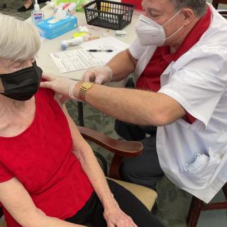 A healthcare professional administers a vaccine to an elderly person wearing a mask.