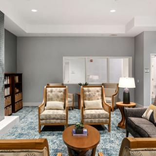 A cozy living room with comfortable armchairs, a central table, and a bookshelf against a gray wall.