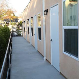 A view of a building's exterior featuring multiple doors and windows along a concrete walkway.