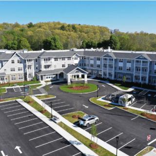 Aerial view of a large residential building with surrounding greenery and a parking lot.