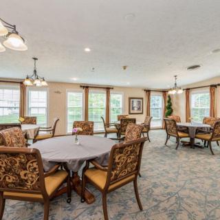A spacious dining room with elegantly set tables and chairs, featuring large windows and decorative lighting.