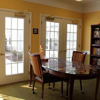 A cozy reading room with a wooden table, chairs, and a bookshelf next to glass doors.