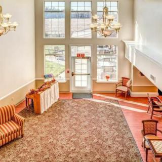 A spacious hotel lobby featuring large windows, elegant chandeliers, comfortable seating, and a patterned carpet.