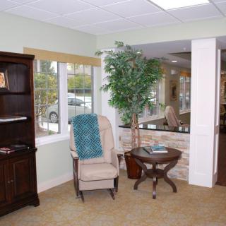 A cozy living room corner with a chair, small table, and bookshelf beside a window.