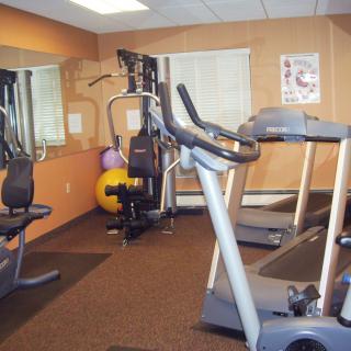 A small gym space with various exercise equipment including treadmills, a stationary bike, and exercise balls.