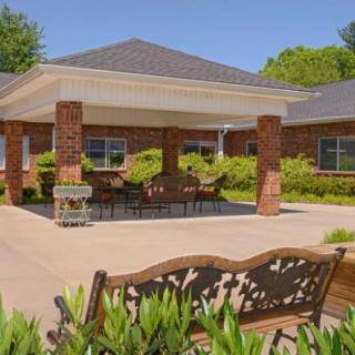 A sunny patio area with a bench and tables outside a brick building.