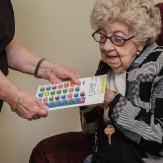 An elderly woman receives a colorful remote control from another person.